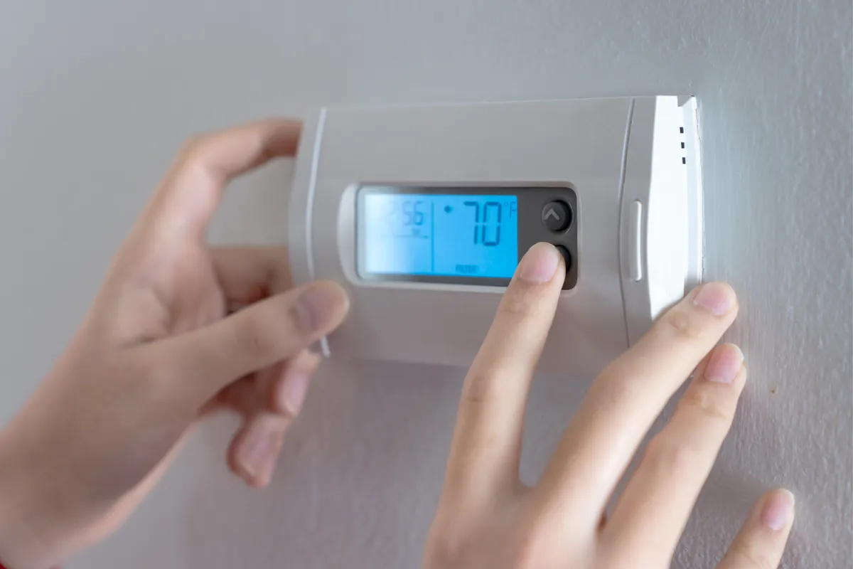 Hands adjusting a digital wall thermostat